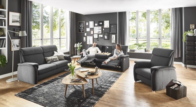 Wohnzimmer mit schwarzer Wand, an der viele Fotos hängen und schwarzen Polstermöbeln
