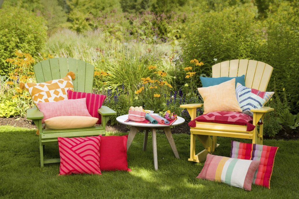 Zwei Gartenstühle aus Holz in Gelb und Grün in einem Garten mit bunten Kissen