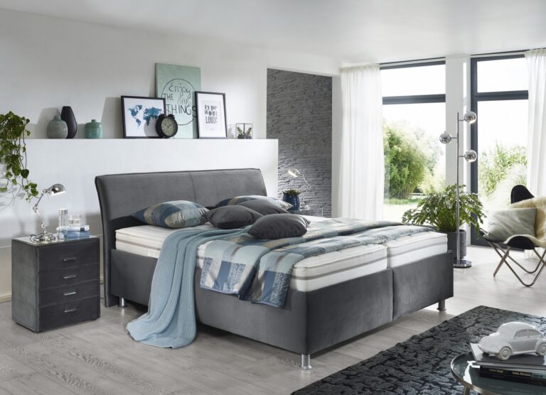 Graues umgepolstertes Bett mit zwei Matratzen und verschiedenen Kissen