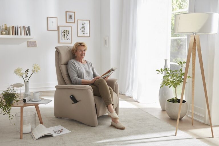 Ältere Dame auf einem Sessel in einem hellen Zimmer, sie liest eine Zeitschrift