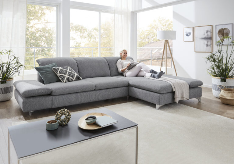 Graue Couch, eine Frau liegt auf dieser und liest ein Magazin