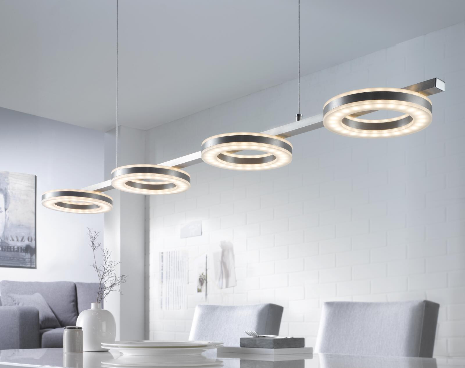 Moderne LED-Pendelleuchte mit vier runden Lichtern über einem Esstisch.