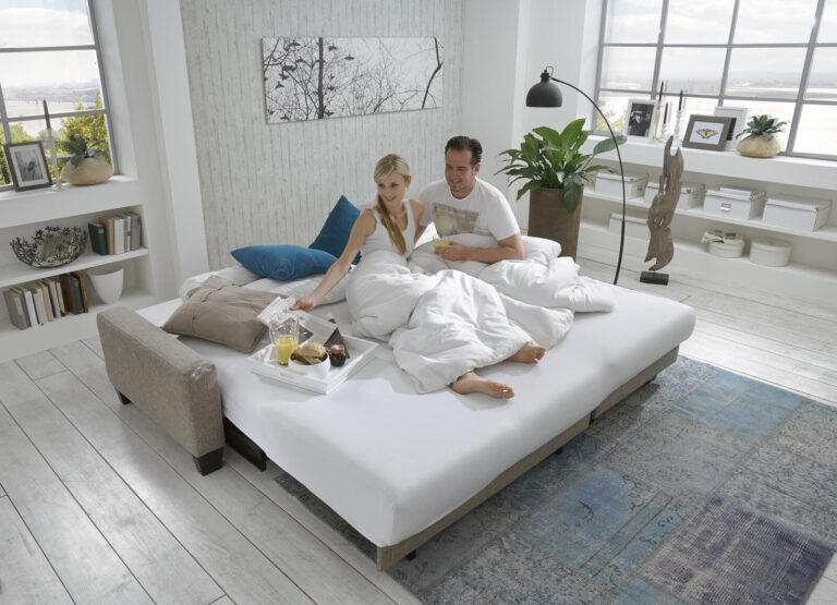 Paar entspannt im Bett und genießt das Frühstück in einem modernen Schlafzimmer.
