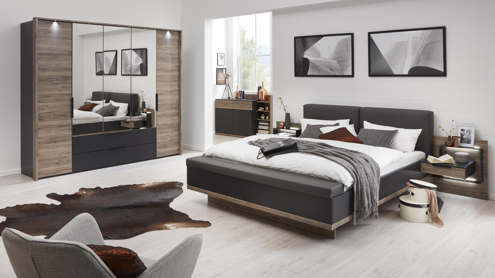 Modernes Schlafzimmer mit grauem Polsterbett, Kleiderschrank aus Holz und Schwarz und Kuhfellteppich.