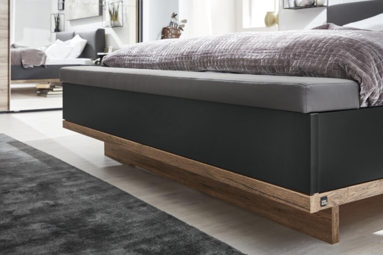 Modernes Plattformbett mit dunkelgrau gepolstertem Kopfteil und Holzsockel.