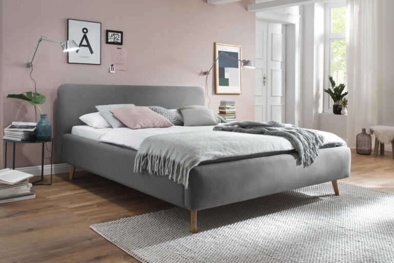 Grau gepolstertes Plattformbett mit hellgrauer Decke und Kissen in einem modernen Schlafzimmer.