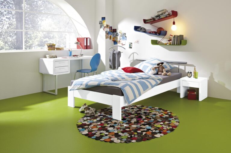 Modernes weißes Kinderzimmer mit grünem Boden, weißem Bett, Schreibtisch und buntem Teppich.