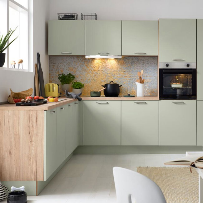 Moderne Küchenschränke in Salbeigrün mit Arbeitsplatten aus hellem Holz und strukturierter Küchenrückwand.