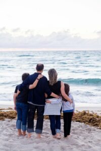 Eine vierköpfige Familie umarmt sich am Strand und genießt die Sommerferien.