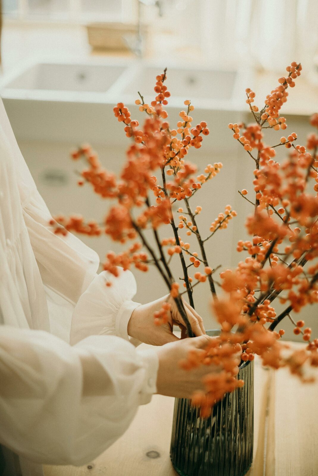 Person arranging branches of orange berries in a dark vase. Erntedankfest decoration.
