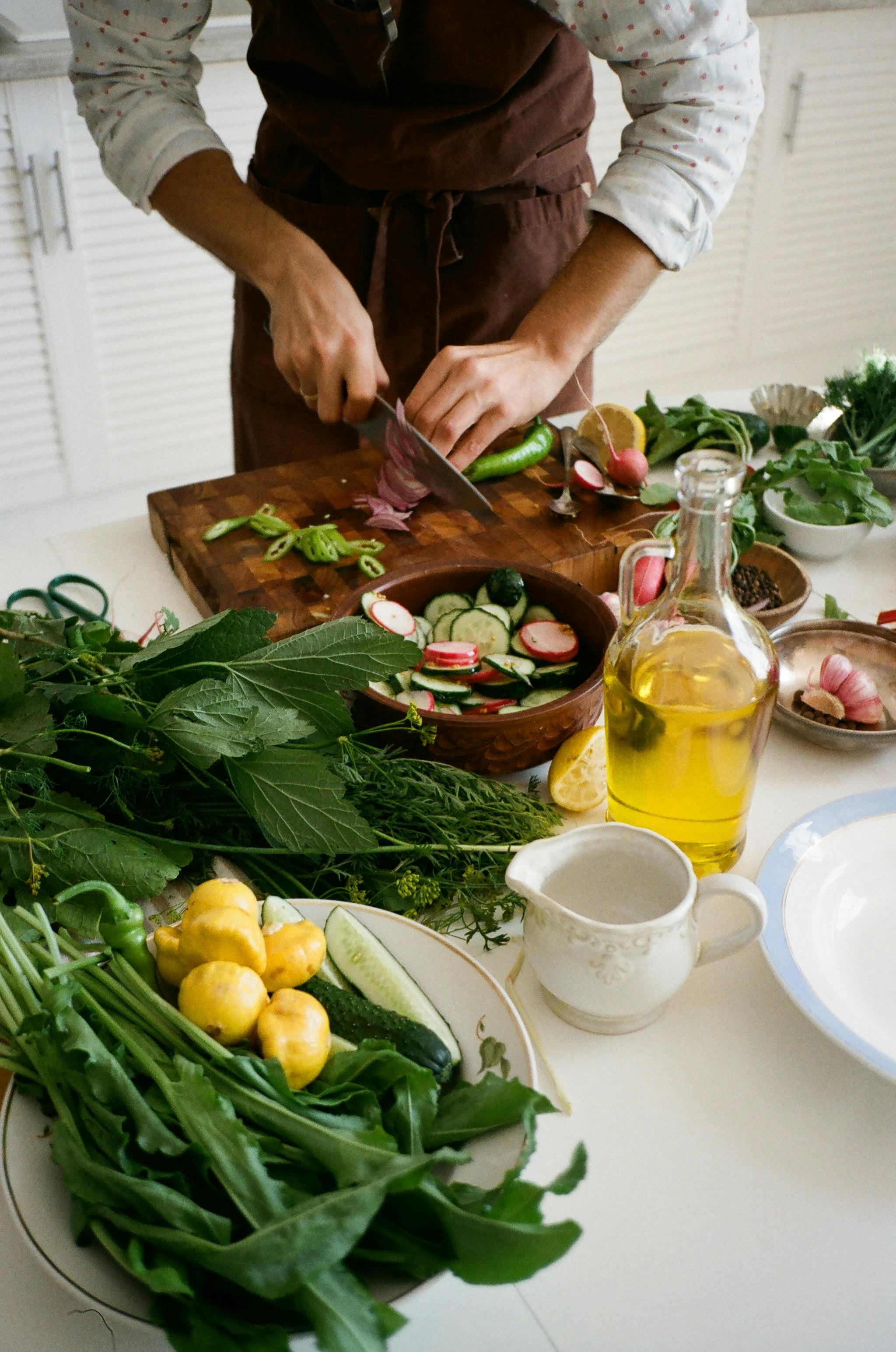 Person preparing a fresh salad with cucumbers, radishes, and herbs for an Erntedankfest dinner.