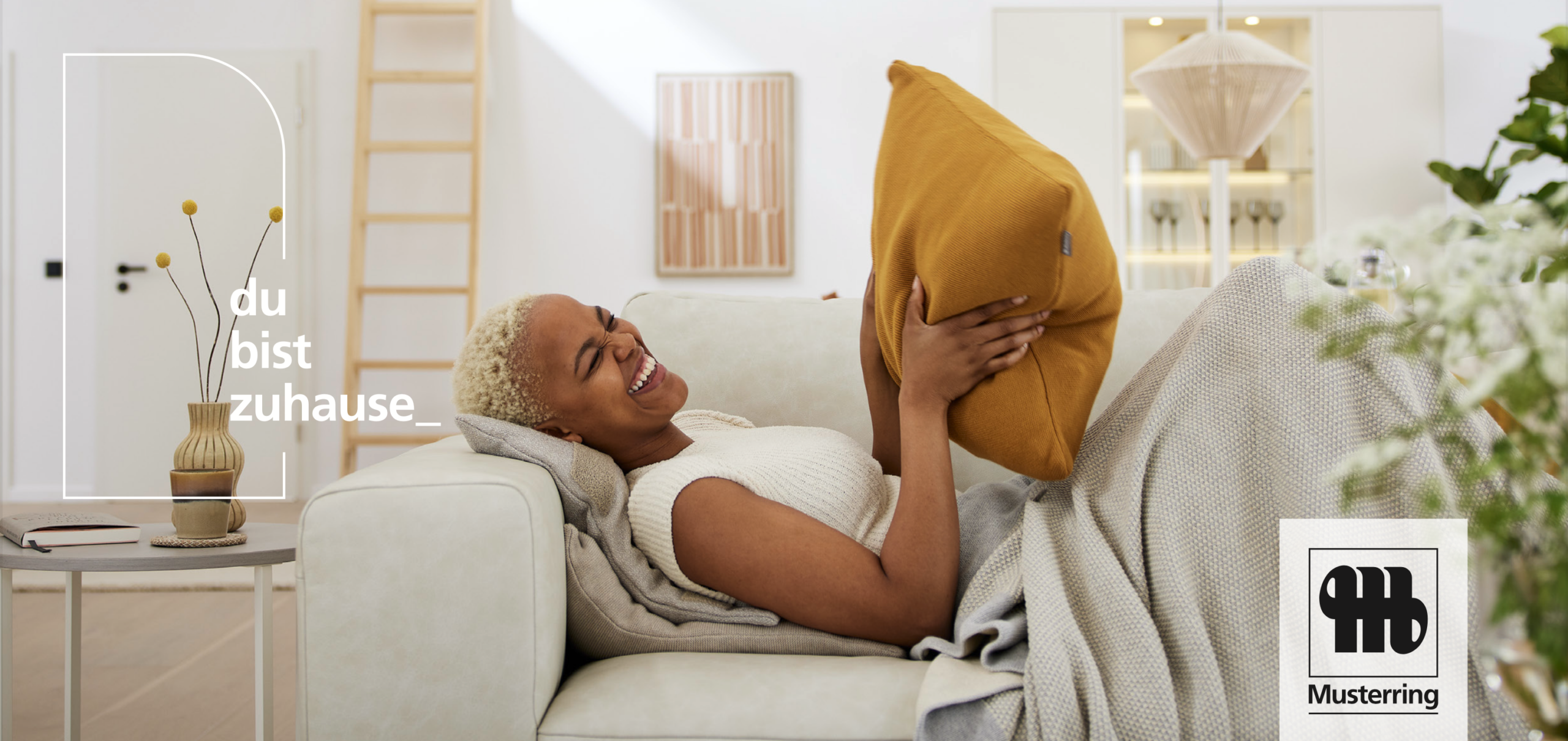 Frau liegt auf einer weißen Couch und hat ein senfgelbe Kissen in der Hand; Sie lacht