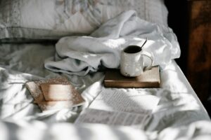 Tasse mit Kaffee und ein Buch auf dem Bett, ideal für Achtsamkeit