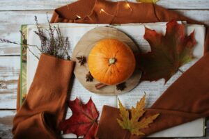 Herbstliche Deko: Kürbis, Blätter, Buch und warmer Pullover für ein gemütliches Zuhause.