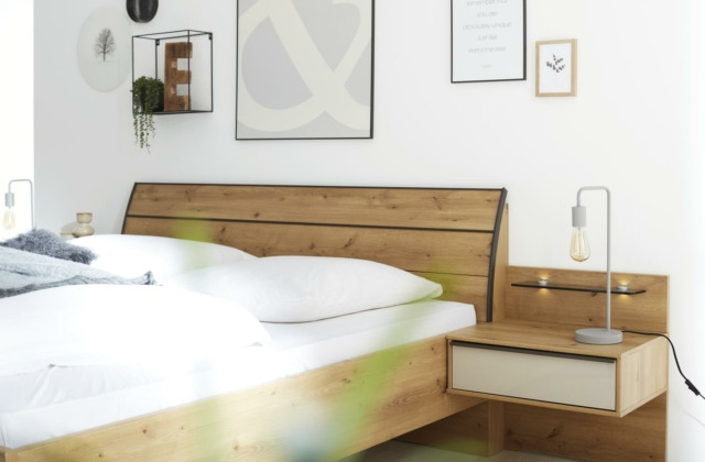 Holzbett mit Nachttisch und Lampe in einem hellen Schlafzimmer