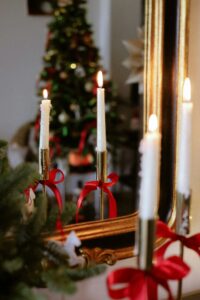 Festliche Dekoration: Kerzenleuchter mit roten Schleifen vor Spiegel, Weihnachtsbaum im Hintergrund.