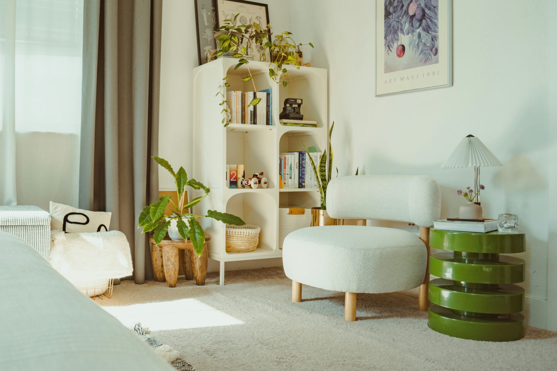 Gemütliches Wohnzimmer mit weißem Sessel, Bücherregal und Pflanzen. Frische Deko für den Frühling.