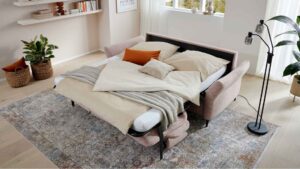 Ausgeklapptes Schlafsofa mit Kissen und Decke im Wohnzimmer.